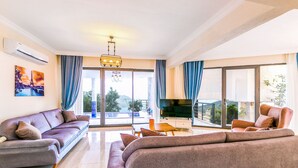 A modern living room with a sofa, a chair, a TV, and a balcony with a view. - Villa Spring - Hill Villas Kalkan (Kas)