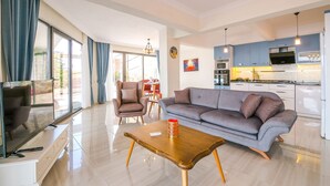A modern living room with a sofa, a coffee table, and a TV. There is a kitchen area with cabinets and appliances. - Villa Spring - Hill Villas Kalkan (Kas)