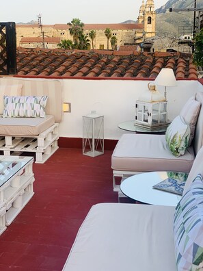 A rooftop terrace with a red-tiled roof, white furniture, and a view of a historic building with a bell tower. - Palazzo del Poeta (Palermo)