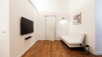 A hallway with a flat-screen TV mounted on the wall, a white sofa, and a framed picture on the wall.