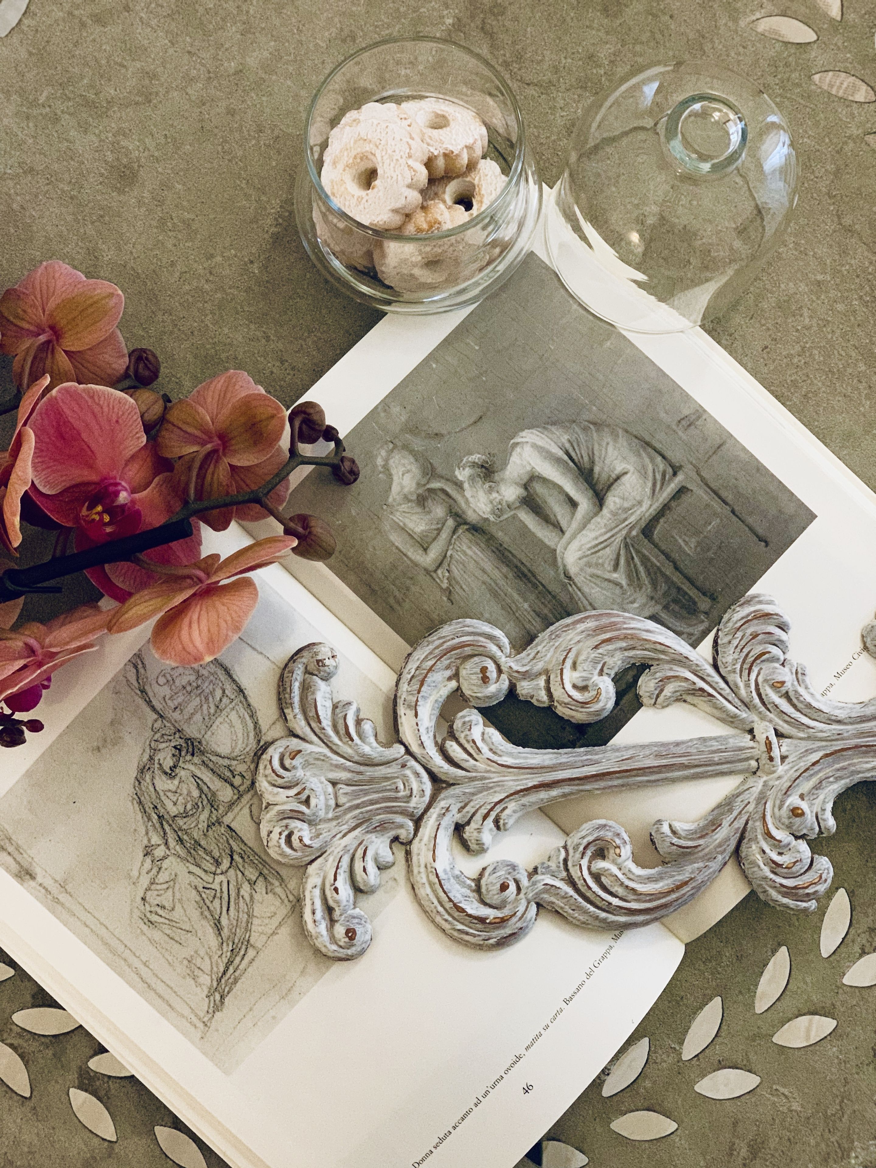 A table with a book, a glass of sugar cubes, and a decorative metal piece.