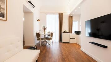 Una sala moderna con un sofá, un comedor con sillas y una mesa, una cocina con televisor y un ventanal con cortinas.