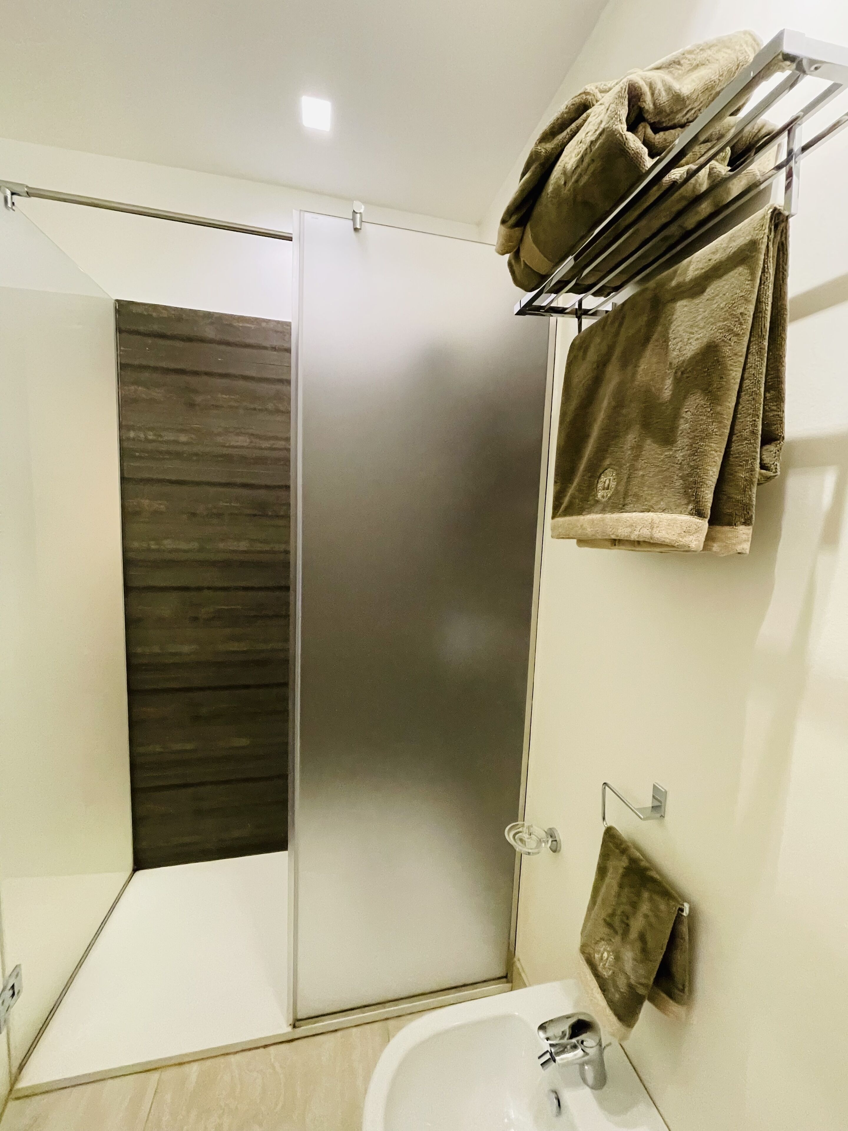 Un baño moderno con cabina de ducha de vidrio, un lavabo blanco y un perchero con toallas.