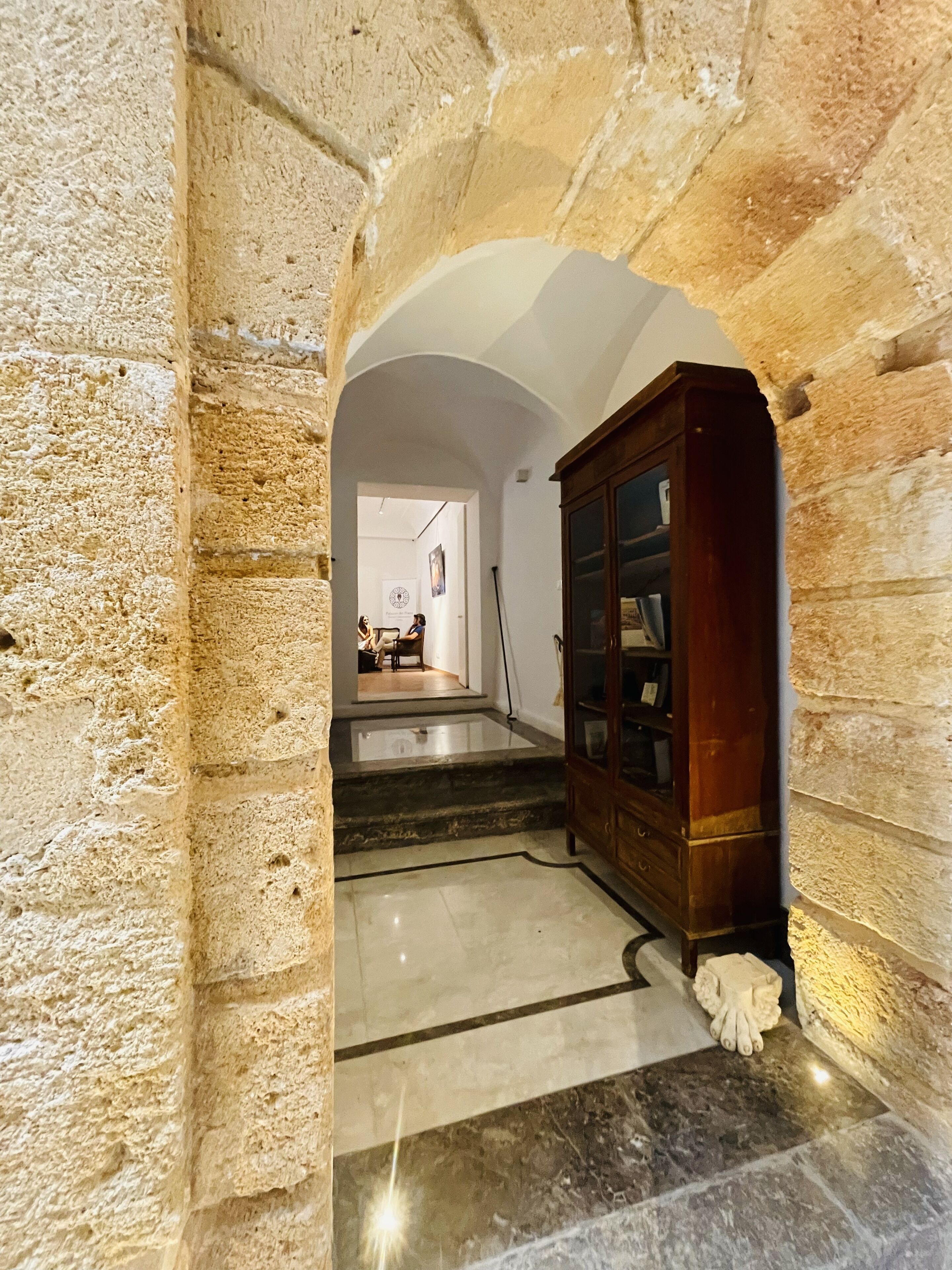 Un arco de piedra que conduce a una escalera con un armario de madera y una escultura blanca.