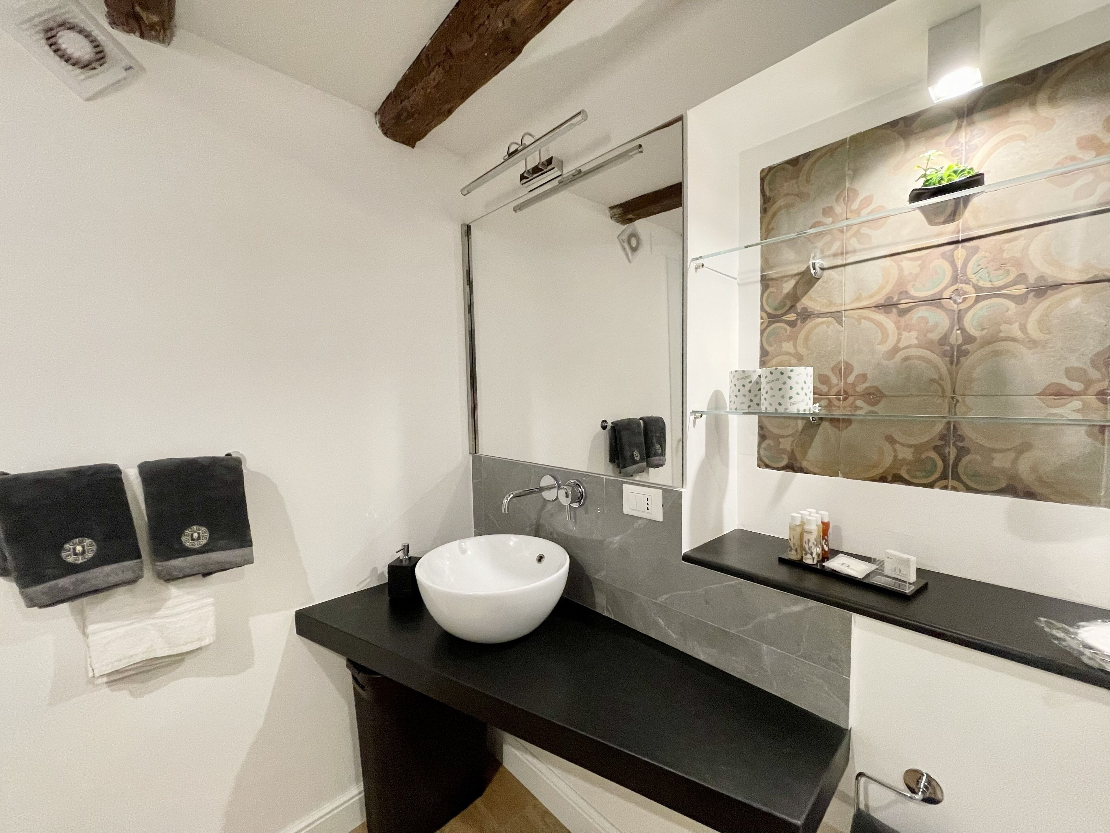 Une salle de bain avec un lavabo blanc, un plan de toilette noir et un miroir agrémenté d’un décor mural.