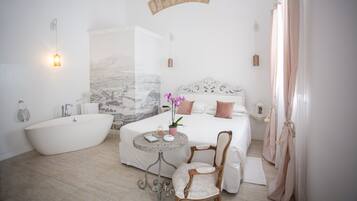A modern bedroom with a large bed, a bathtub, a round table with a chair, and a decorative wall piece.