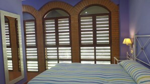 Une chambre à coucher avec un lit, un miroir et trois fenêtres en arc surmontées de stores.