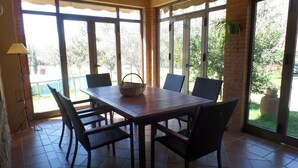 Un coin repas avec une table en bois et quatre chaises, de grandes fenêtres et une plante en pot.