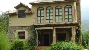 Une maison à deux étages avec une façade en pierre, de grandes fenêtres en arc de cercle et un toit recouvert de tuiles.