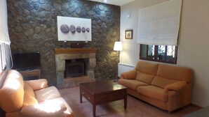 Un salon avec un mur en pierre, une cheminée, un canapé, une table basse et un téléviseur.
