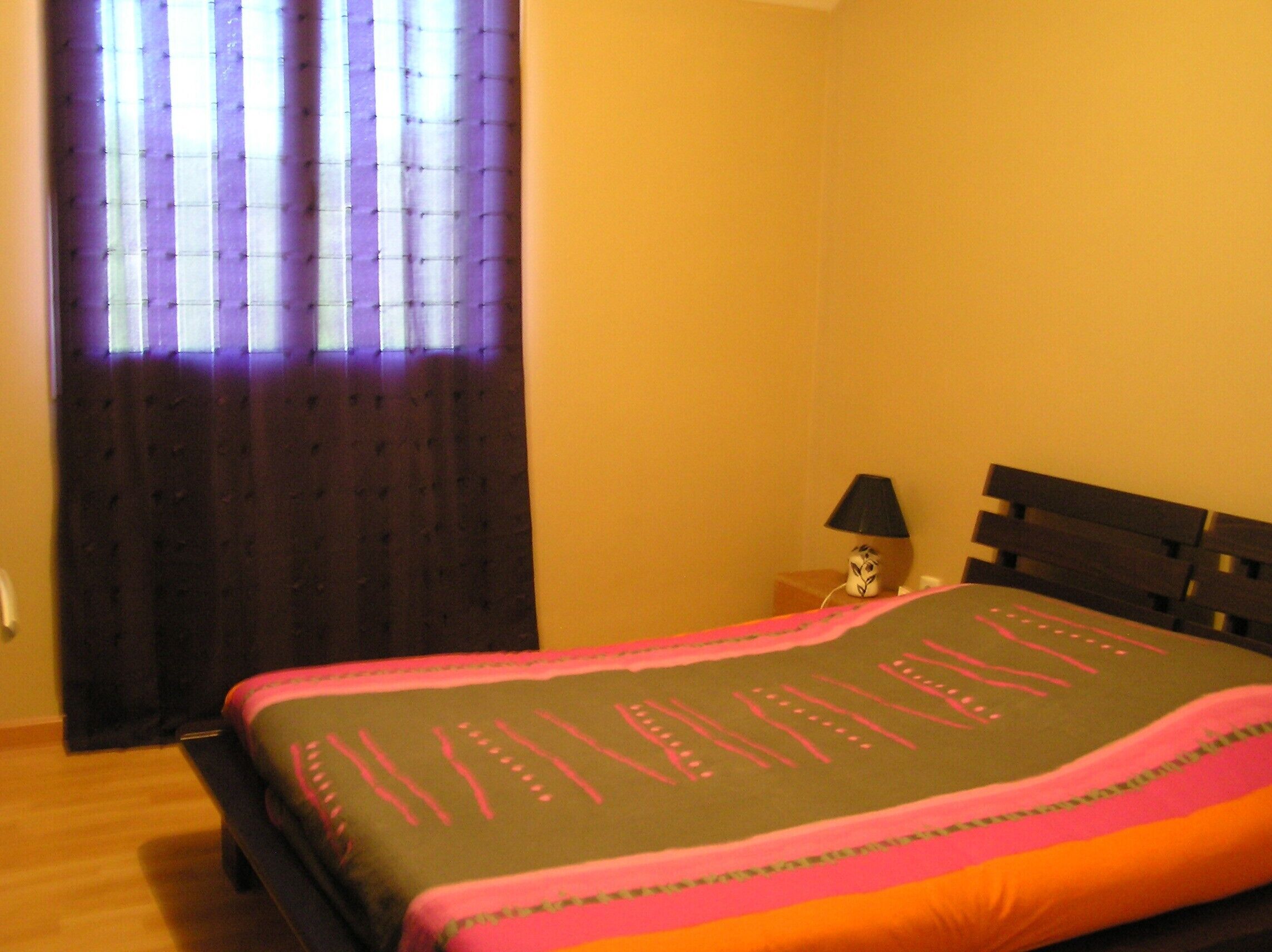 A bedroom with a bed, a nightstand, a lamp, and a window with curtains.