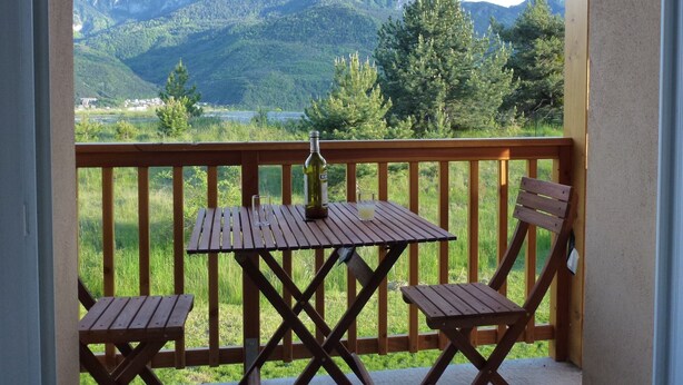 Un balcon avec une table en bois et deux chaises, donnant sur un paysage montagneux.