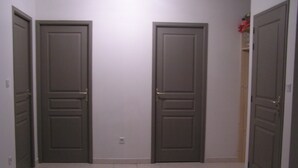 Un couloir avec deux portes fermées, un sol carrelé et un interrupteur sur le mur.