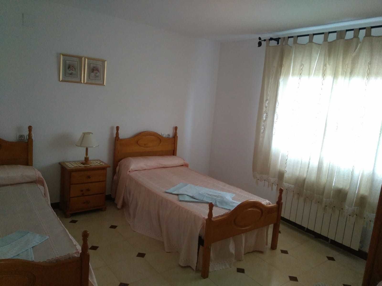 Ein Schlafzimmer mit zwei hölzernen Betten, einem Nachttisch mit Lampe, einem Heizkörper und einem Fenster mit Vorhängen.