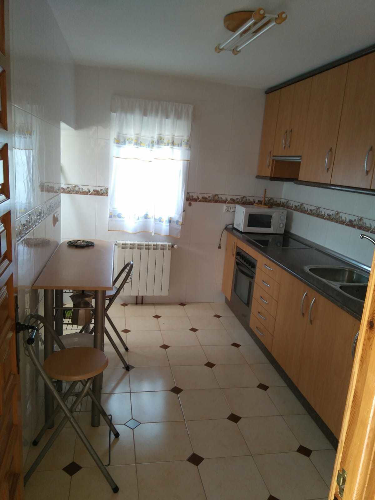 A compact kitchen with wooden cabinets, a microwave, a sink, and a dining area with a chair and table.