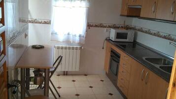 A compact kitchen with wooden cabinets, a microwave, a sink, and a dining area with a chair and table.