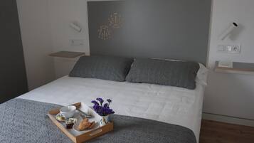 Un lit bien fait, avec une literie grise, un plateau contenant des éléments de petit-déjeuner et un objet décoratif accroché au mur.