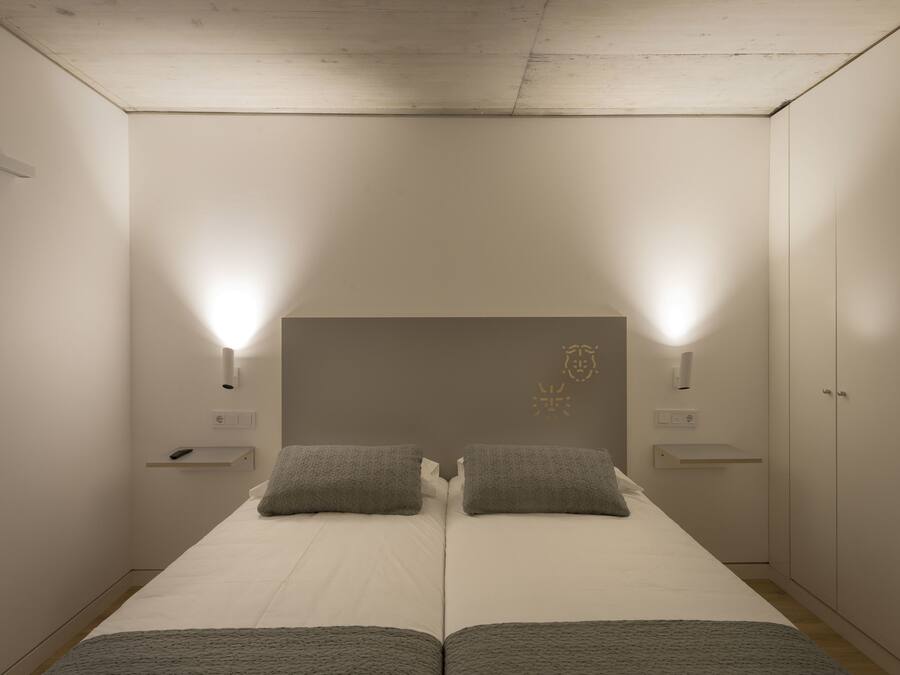 A bedroom with a double bed, two bedside tables, a wardrobe, and a headboard with a crest.