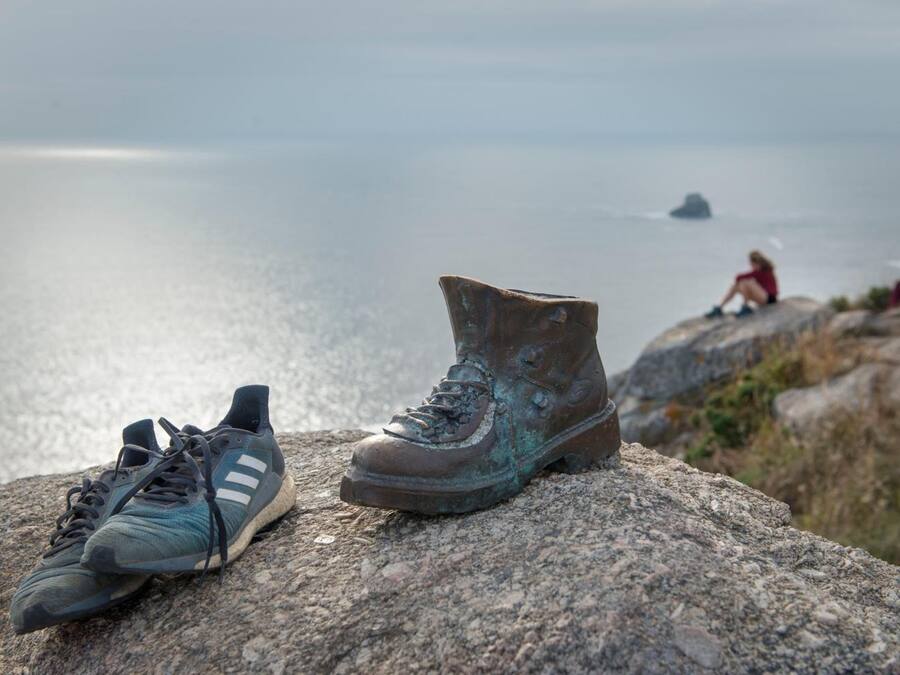 A pair of shoes on a rock with a view of the sea and a person in the background.