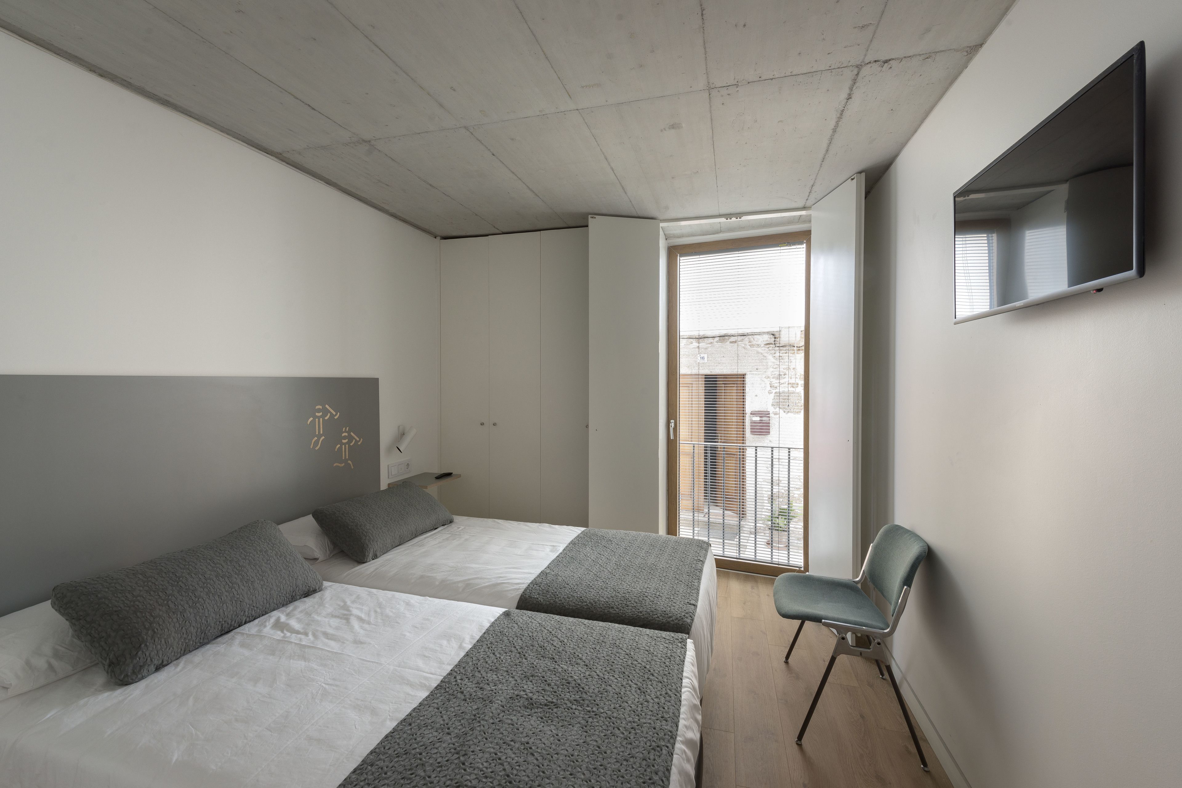 A bedroom with two beds, a chair, a TV, and a balcony.