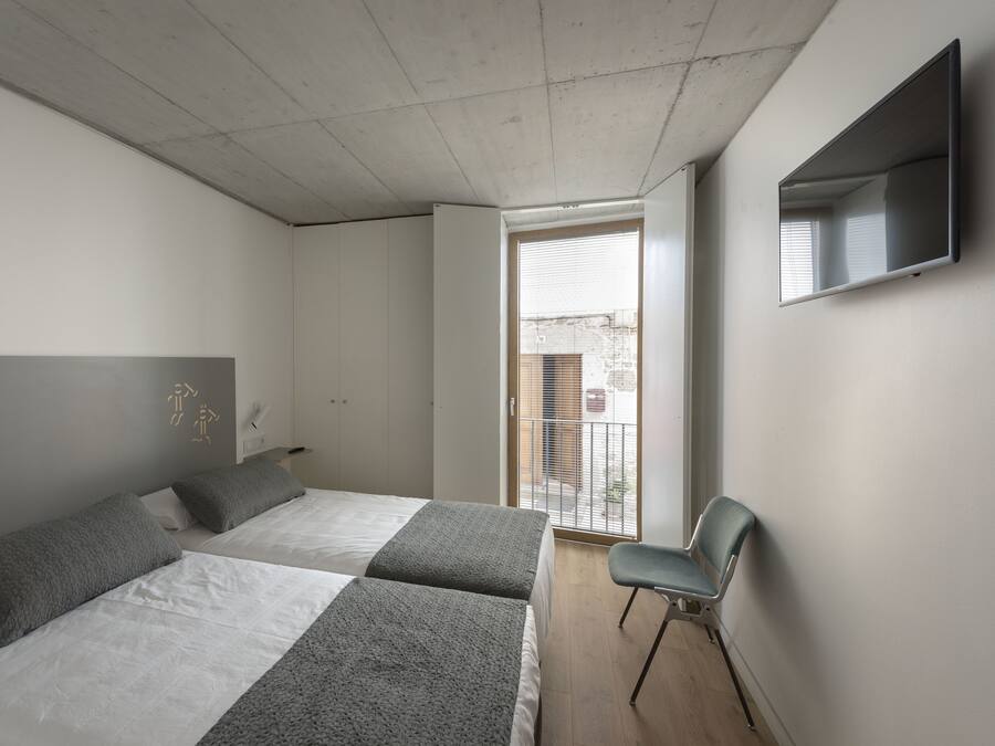A bedroom with two beds, a chair, a TV, and a balcony.