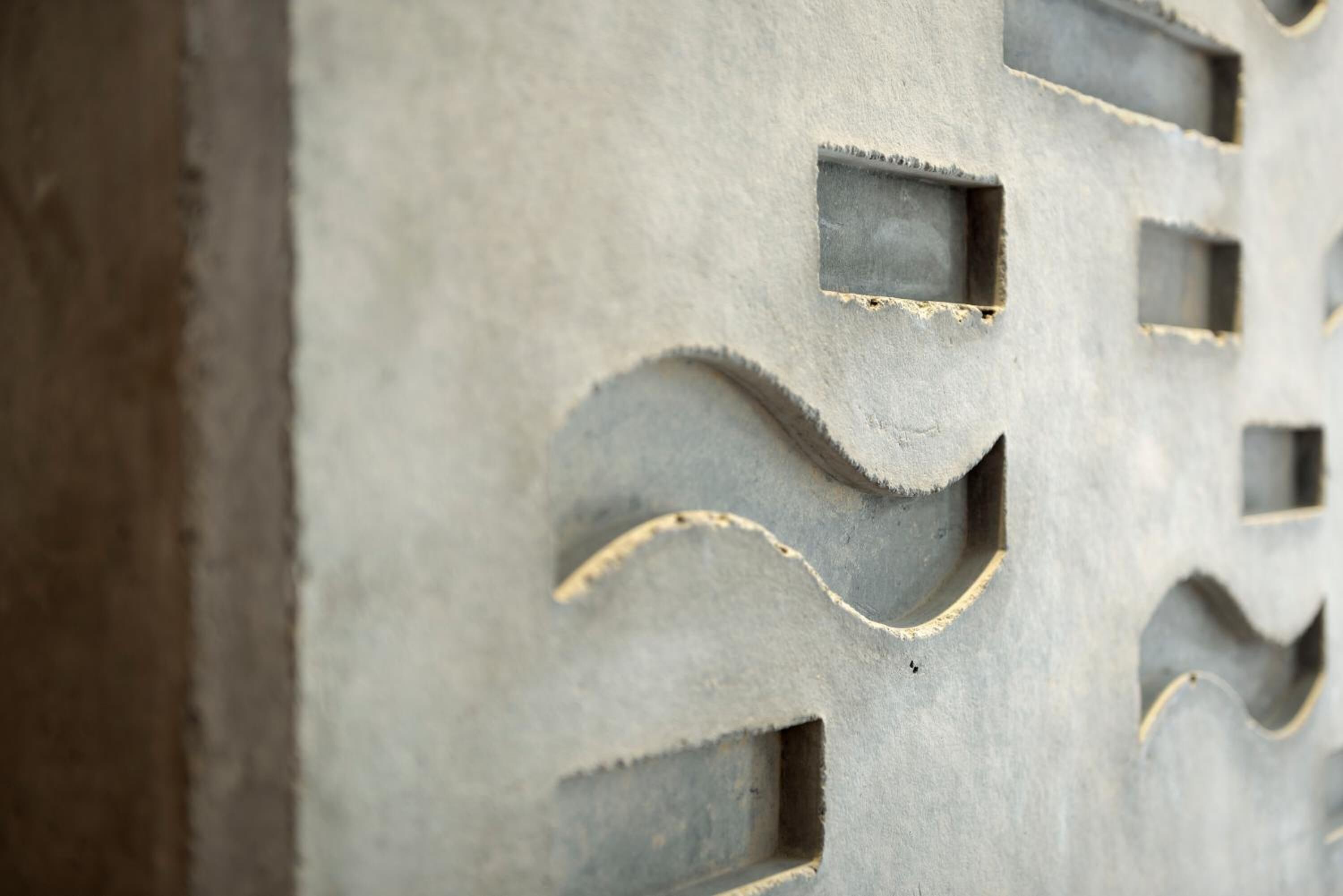 A close-up of a textured concrete wall with rectangular cutouts and curved indentations.