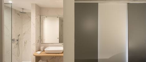 Un baño moderno con cabina de ducha de vidrio, zona de ducha con azulejos de mármol, tocador de madera con lavabo y un taburete pequeño.