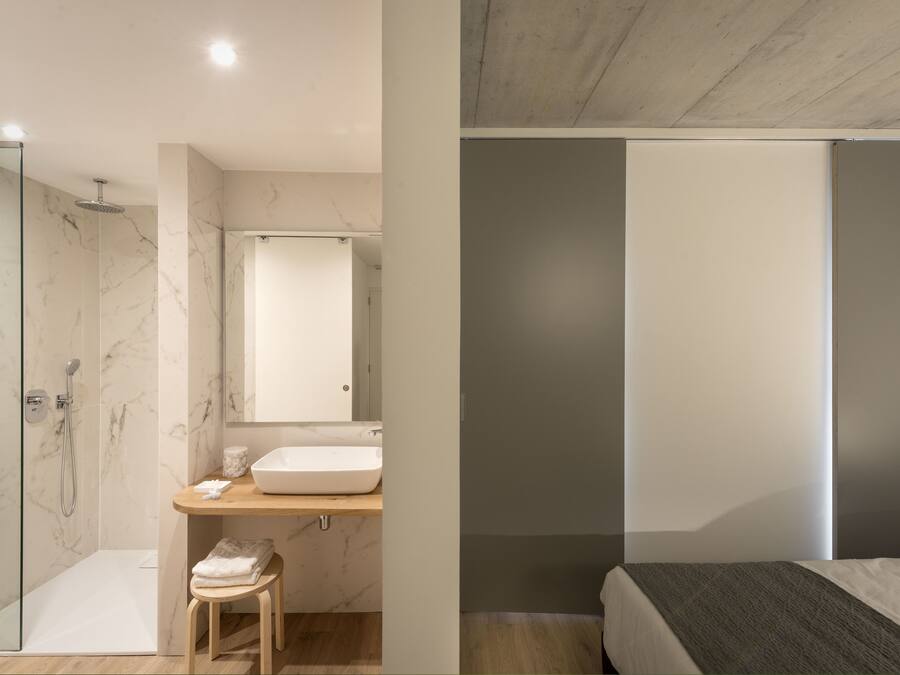 A modern bathroom with a glass shower enclosure, a marble-tiled shower area, a wooden vanity with a sink, and a small stool.