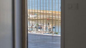 A room with a large window overlooking a harbor, a view of boats, and a distant mountain range. - Hotel SempreFisterra (Fisterra)