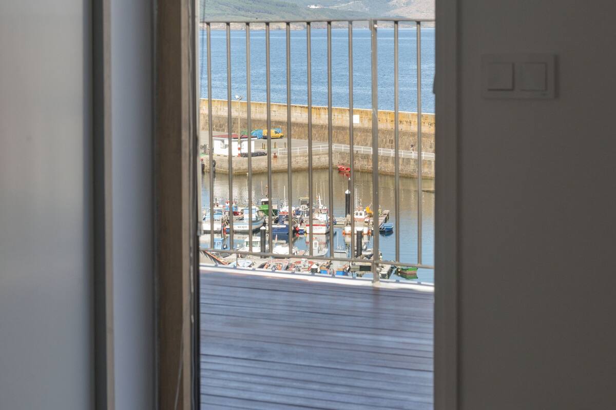 A room with a large window overlooking a harbor, a view of boats, and a distant mountain range.