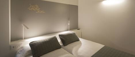 A neatly arranged bedroom with a bed, two bedside lamps, and a wall-mounted light fixture.