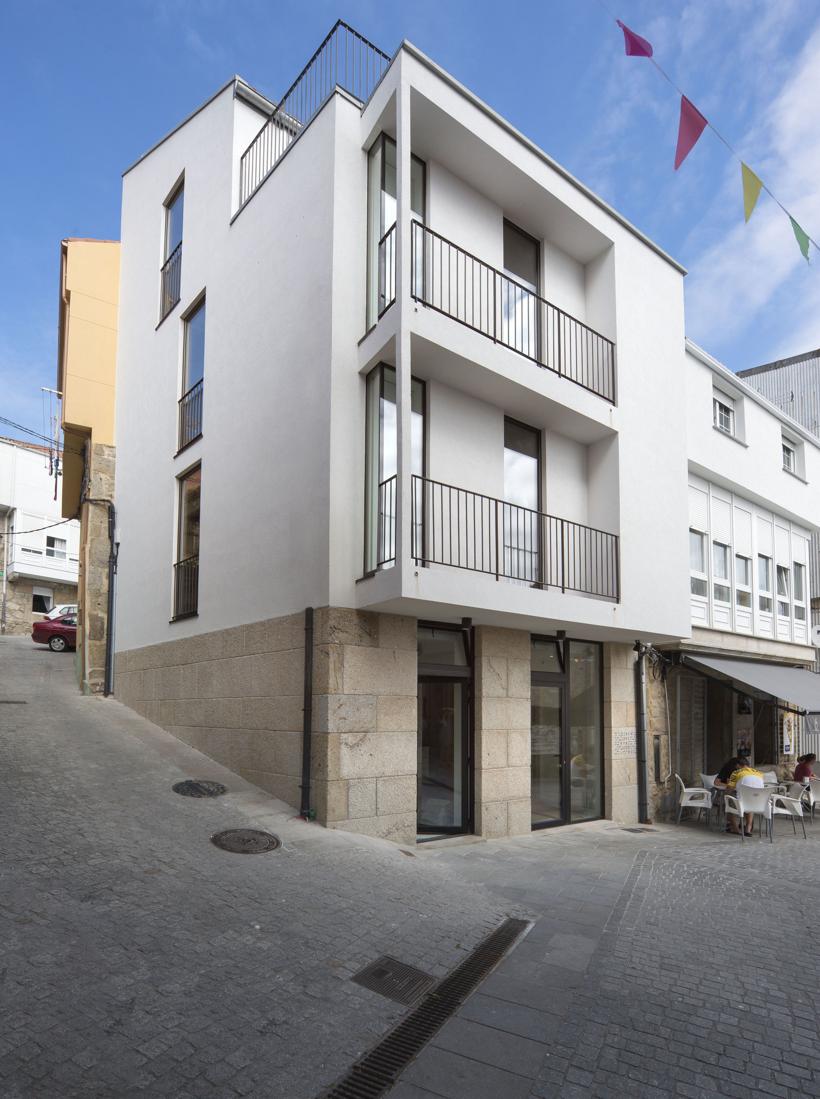 Un edificio moderno con fachada blanca, varios balcones y entrada a nivel de calle con puerta de vidrio.