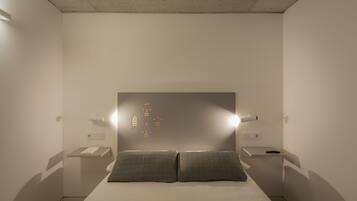 A minimalist bedroom with a bed, bedside tables, and wall-mounted light fixtures.
