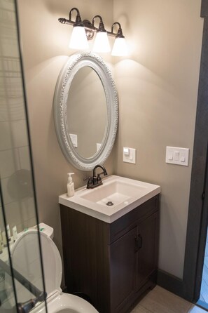 Une salle de bain avec un lavabo blanc, un meuble en bois foncé et un grand miroir doté d’un cadre orné.