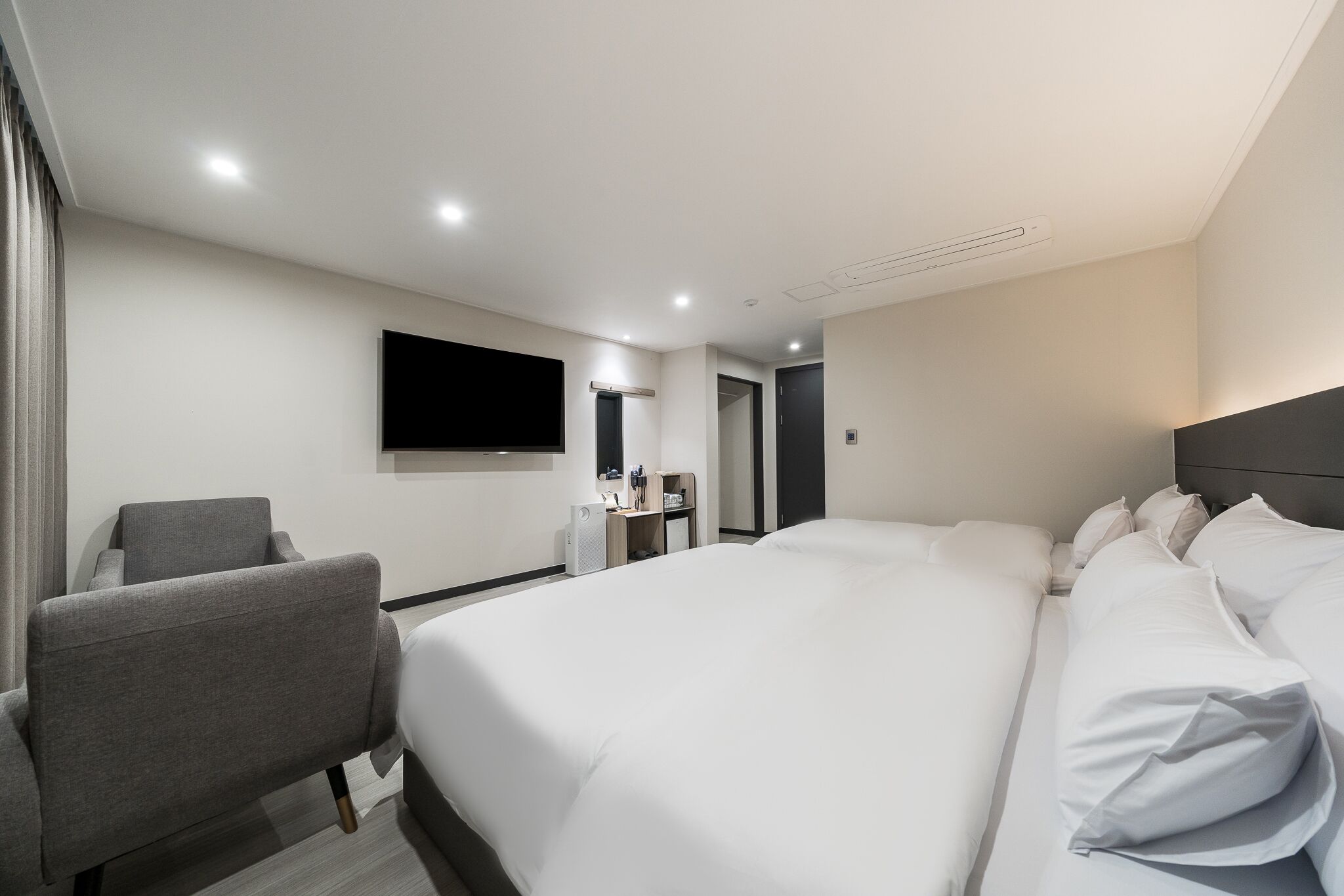 A hotel room with a large bed, a desk with a chair, a flat-screen TV mounted on the wall, and a wardrobe.