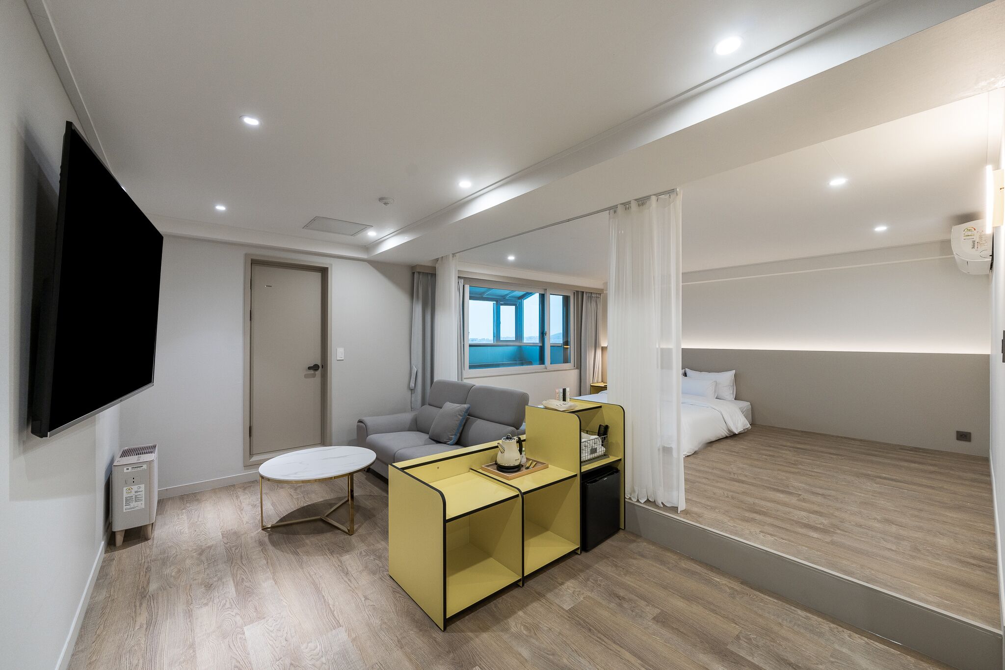 A modern hotel room with a sofa, a small table, a bed, and a TV.