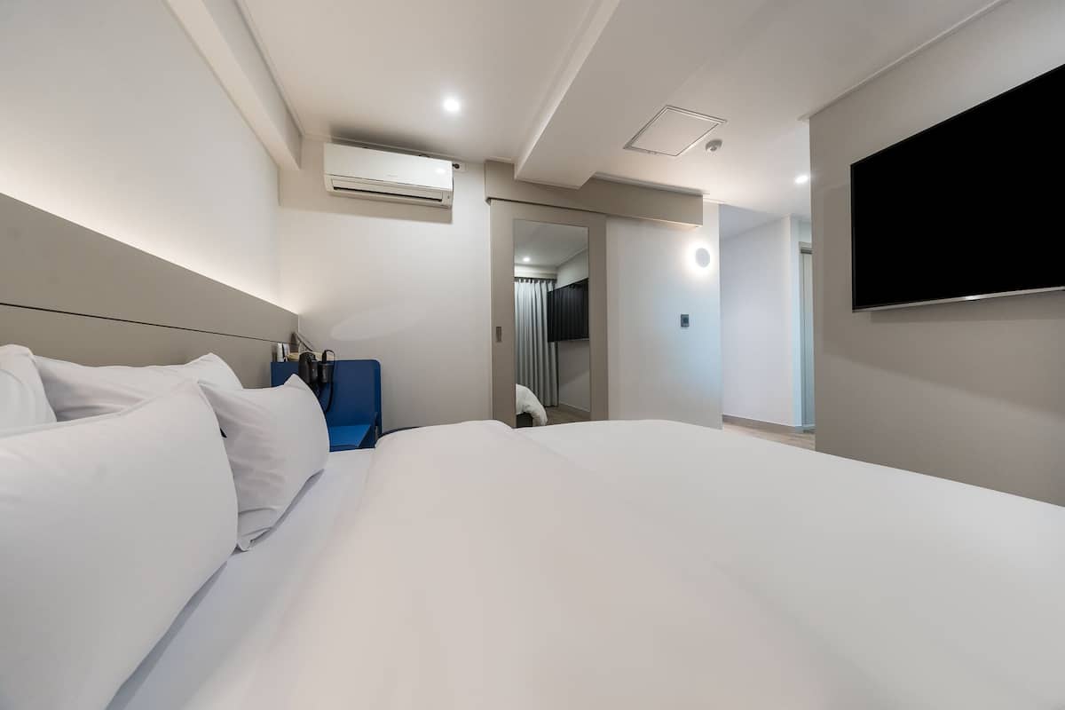A modern hotel room with a large bed, a flat-screen TV mounted on the wall, and a bathroom visible through an open door.