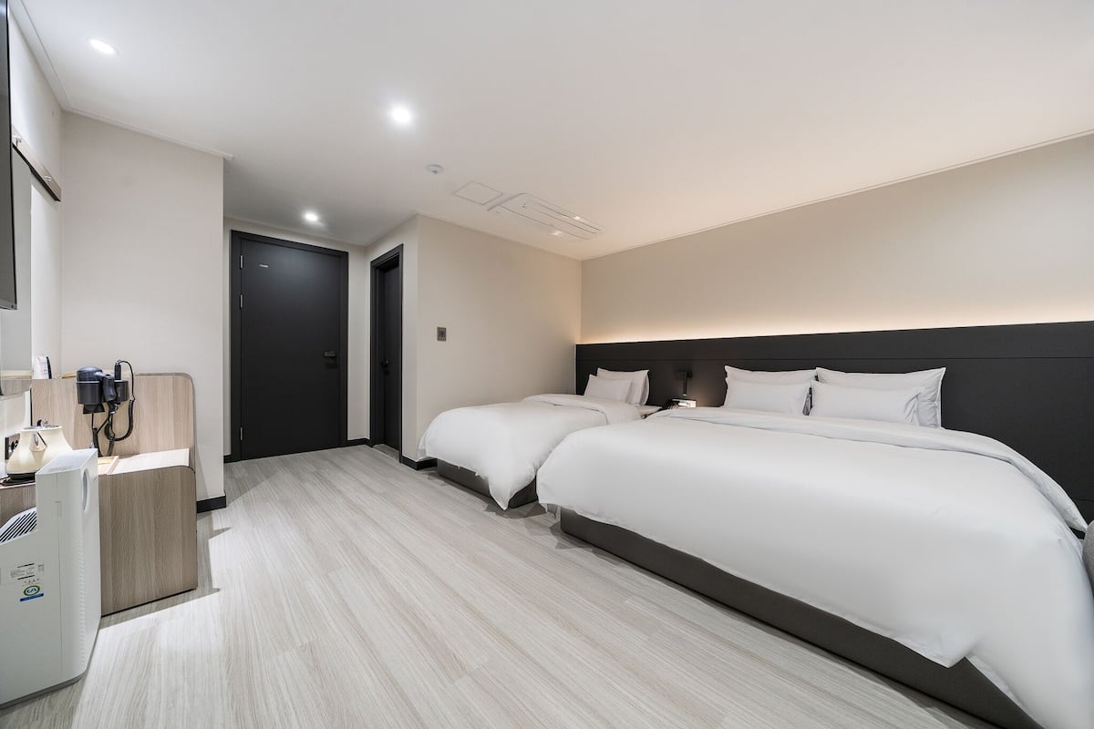 A hotel room with two beds, a desk with a printer, and a door leading to another room.