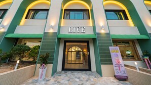 The exterior of the LIV LIFE HOTEL with a prominent entrance, arched windows, and a sign indicating a sale.