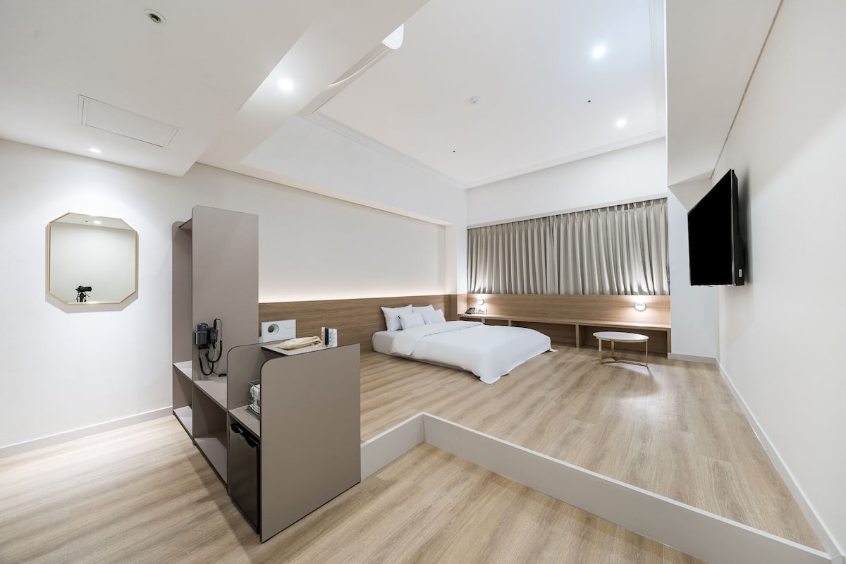 A modern hotel room with a bed, bedside table, TV, and a small seating area.