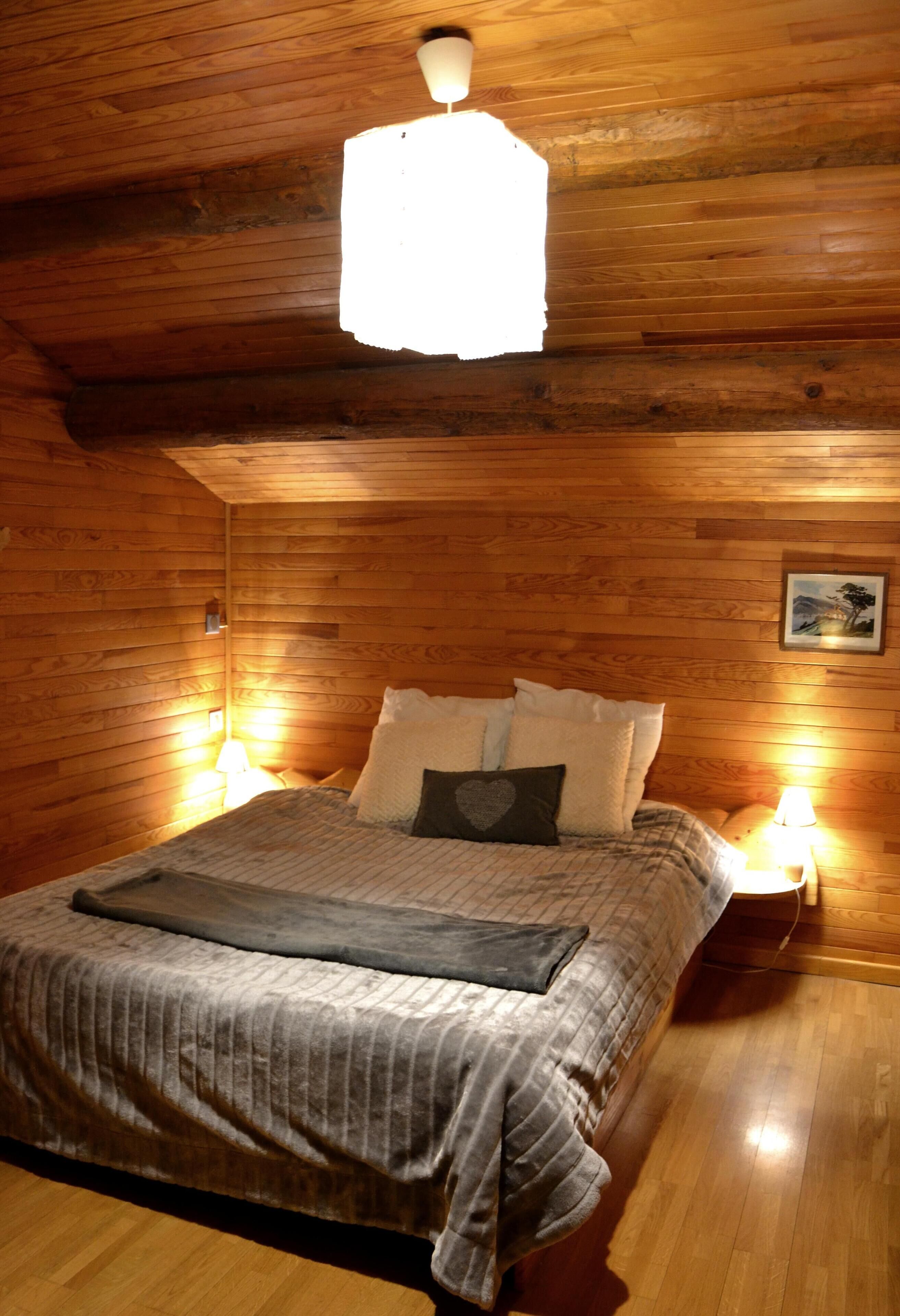 A cozy wooden room with a bed, two bedside lamps, and a hanging light fixture.