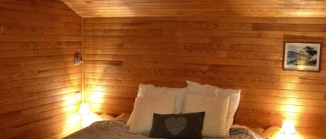 A cozy wooden room with a bed, two bedside lamps, and a hanging light fixture.