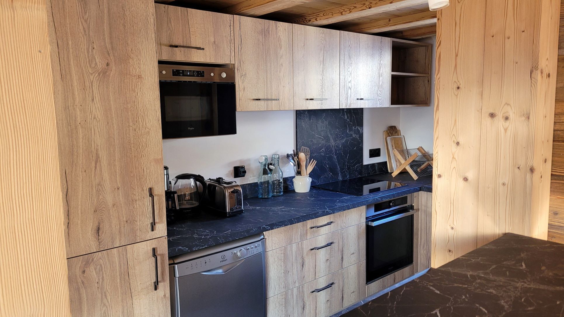 A modern kitchen with wooden cabinets, a built-in oven, a dishwasher, and a marble countertop.