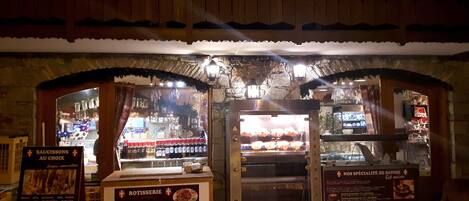A bakery with a rustic stone facade, open display cases, and signs advertising various baked goods and prices.