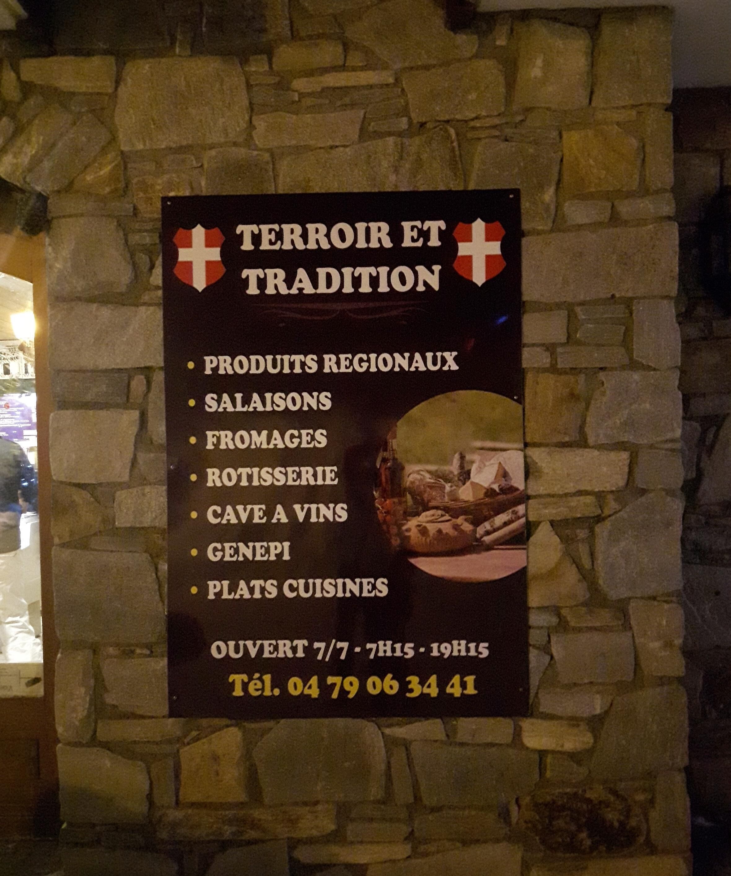 Une enseigne fait la publicité de « Terroir et Tradition », proposant des produits régionaux, des salades, du fromage, des plats de charcuterie, une cave à vins, du génépi et des plats préparés. Elle est ouverte 7 jours sur 7, de 7 h 15 à 19 h 15.