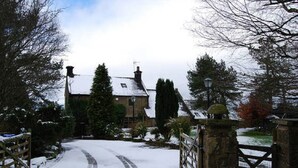 A snow-covered rural road leading to a traditional stone house with a gated entrance.