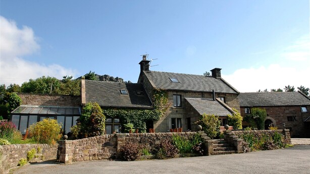 A stone building with multiple chimneys, a large glass conservatory, and a stone wall with plants.