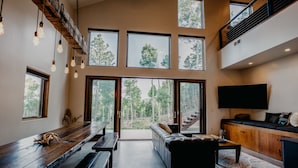 A spacious living area with a long wooden bench, a sofa, and a coffee table. There are multiple windows providing a view of the outdoors. - Gate Access To 1.5 million Acre Carson National Forest! (Angel Fire)