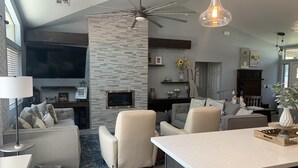 Ein modernes Wohnzimmer mit Kamin, Deckenventilator und großem Fernseher.