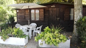 A wooden cabin with a patio area featuring a table and chairs, surrounded by potted plants. - Smeraldo Camping Village (Bracciano)